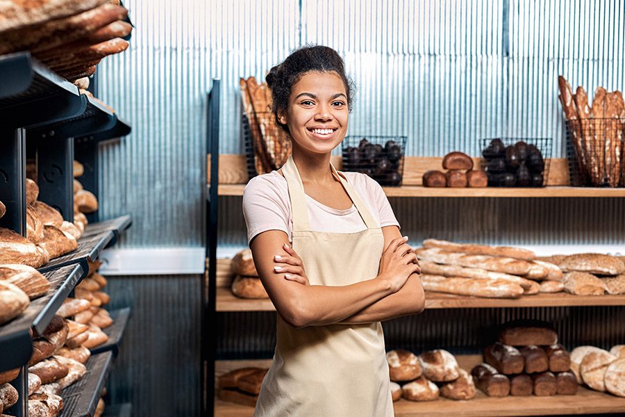 Business Insurance - Smiling Young Adult Woman Standing With Arms Crossed in Family Bakery